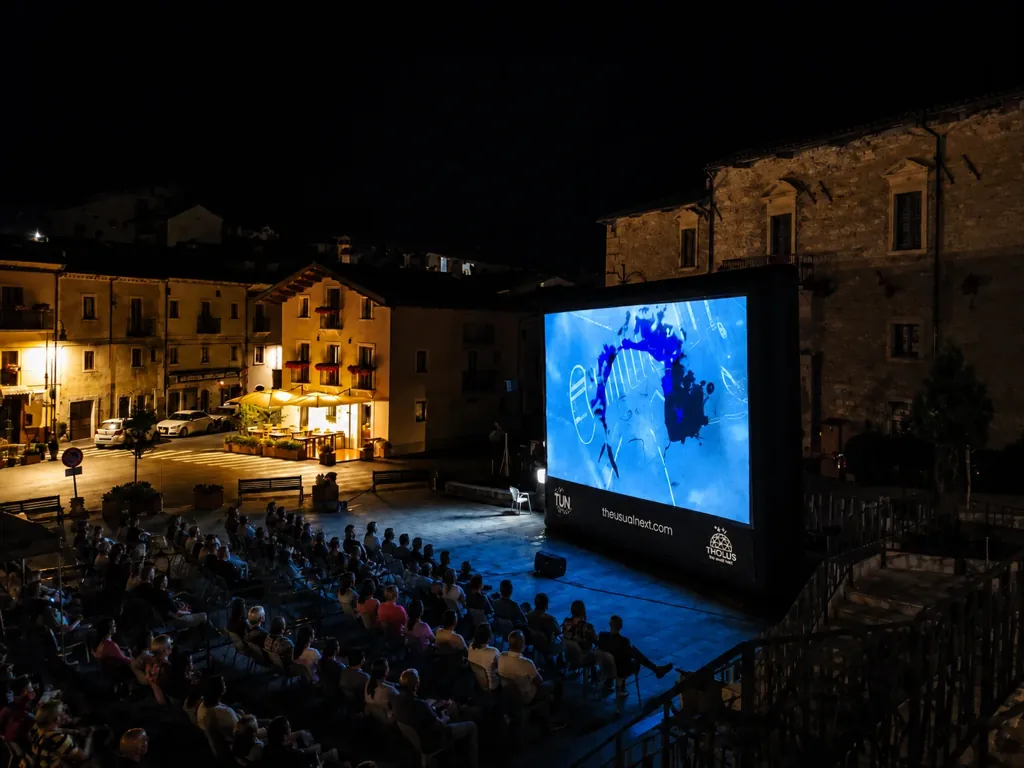 Proiezione cinematografica all’aperto con grande schermo e pubblico