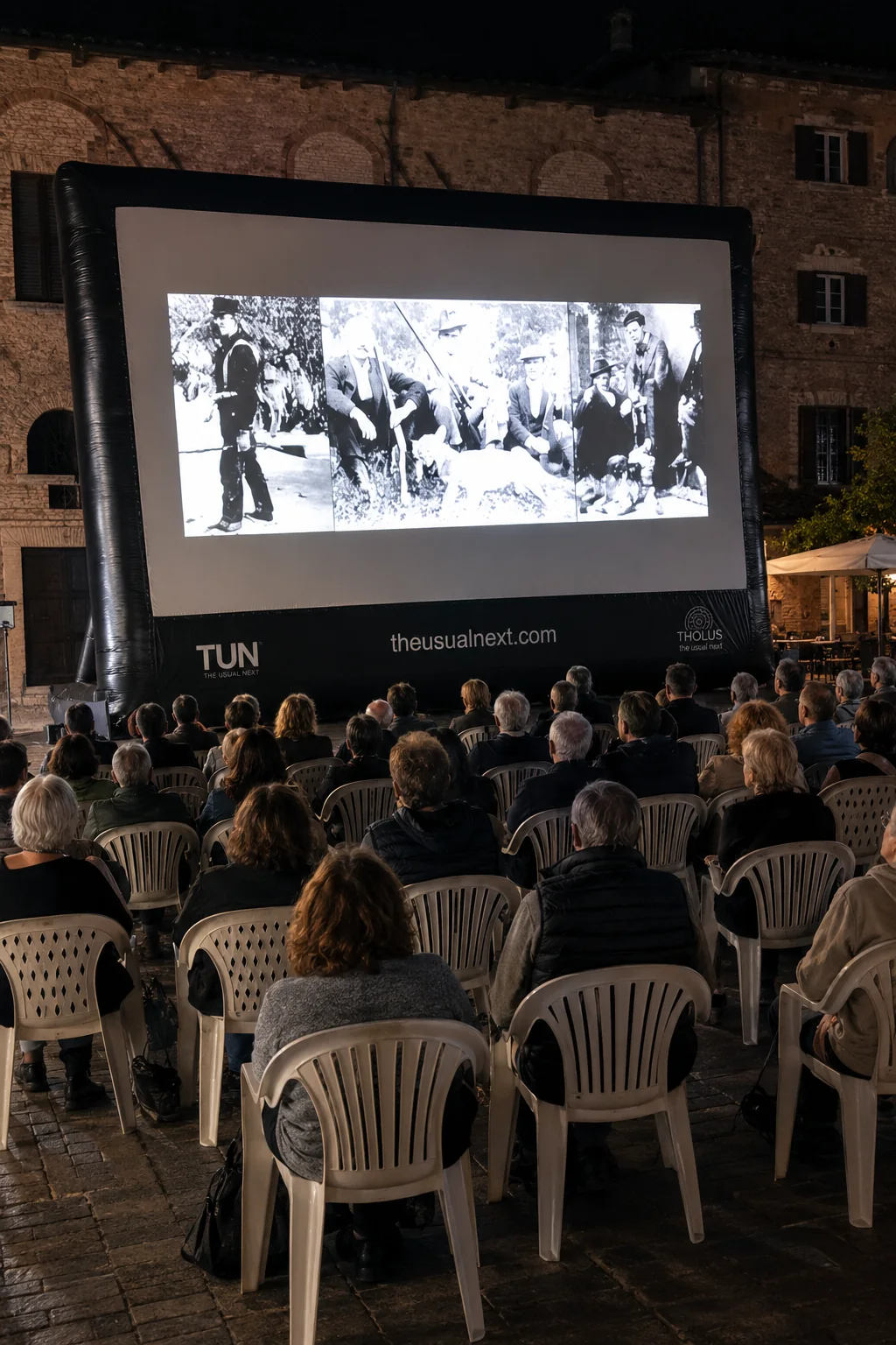 Pubblico seduto davanti allo schermo di un cinema all’aperto in una piazza storica