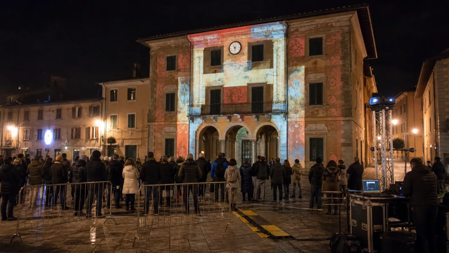 Videomapping su una facciata storica con pubblico e regia tecnica in piazza