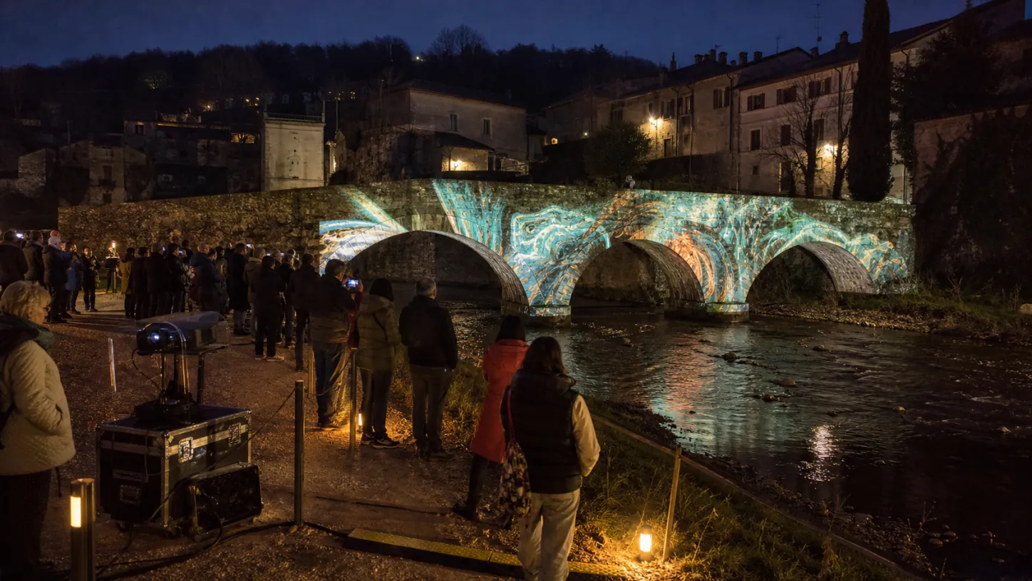 Videomapping su un ponte storico osservato dal pubblico lungo il fiume