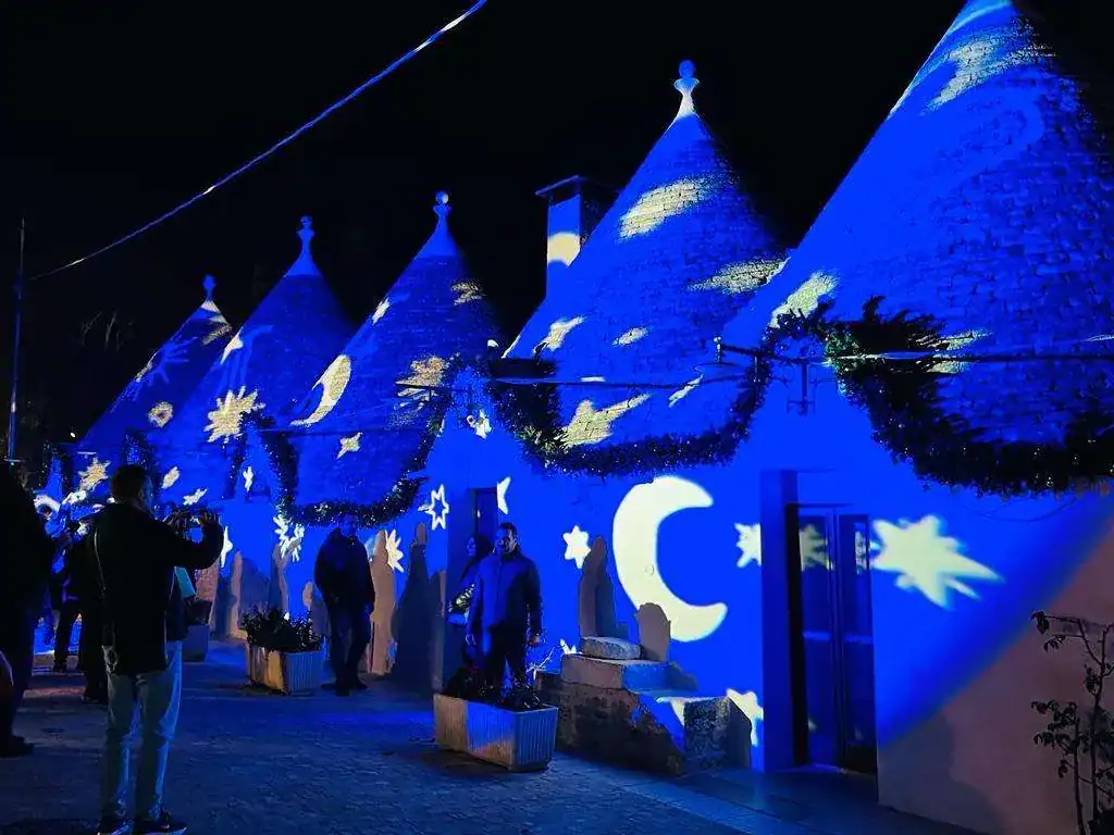 Suggestive lighting di luci blu proiezioni di stelle e lune su tetto di trulli in notturna, evento culturale o decorativo, atmosfera magica e suggestiva, tradizione e innovazione nel design.